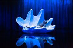 Emil Hedayat ligger i en stor, vit abstrakt snäcka, omgiven av mörkblå belysning.