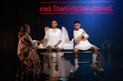 Tre personer i vita kläder sitter på en scen.