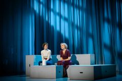 Två kvinnor sitter på en scen med blå belysning.