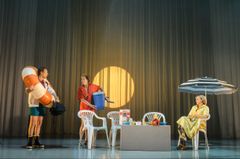 Tre personer på scenen med semestertema framför en kuliss med sol, plaststolar och parasoll.