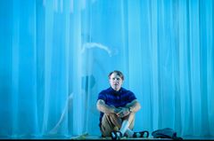 En man sitter på scenen framför ett blått draperi.