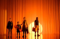 Fyra personer står mot en orange bakgrund med ljus som skapar silhuetter.