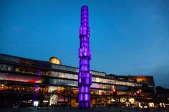 Kulturhuset vid Sergels torg på kvällen med en lysande, lila obelisk.