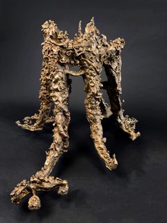 En bronsminiatyr av en komplex lerskulptur med organiska former mot en mörk bakgrund.