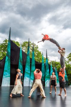 En grupp artister utför en akrobatisk uppvisning utomhus med spetsiga dekorativa bakgrunder.