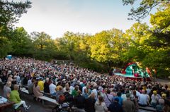 Massa publik som sitter framför en utomhusscen en solig sommardag.