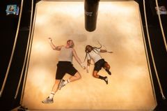 Två personer ligger på en boxningsringmatta, avslappnade med ett slagsäck ovanför.