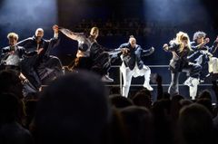 En grupp människor dansar energiskt på scenen i en teaterproduktion.