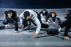 Flera personer rör sig dynamiskt över en scen i modern klädsel.