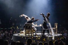 En scenbild från en teaterföreställning med tre skådespelare i dramatiska poser på en cirkulär plattform.