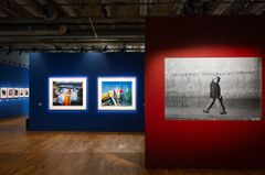 En konstutställning med flera inramade fotografier på blå och röd vägg.