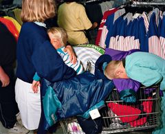 Två barn sover i en kundvagn fylld med kläder i en butik.