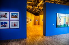 Utställningsvy med konstverk på väggarna i ett galleri, med blå och gul väggfärg.