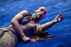 En person i en dramatisk pose på en blå scen.