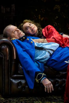 Peter Andersson och Lena Olin ligger på en soffa i scenkostymer från teaterpjäsen "Fadren".