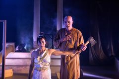 Två skådespelare i dramatisk scenklädsel på en teaterscen. En person håller i en yxa och ser intensivt framåt.