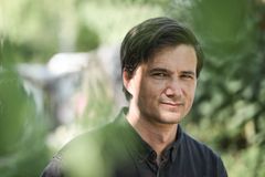 En man med mörkt hår står utomhus, omgiven av gröna blad.