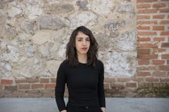 En kvinna i svart tröja står framför en sten- och tegelvägg.