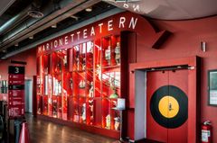 Röd vägg med texten "MARIONETTEATERN" och en dörr med en måltavla i svart och gult.