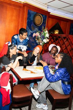 Fem personer sitter runt ett bord och pratar och äter tillsammans.