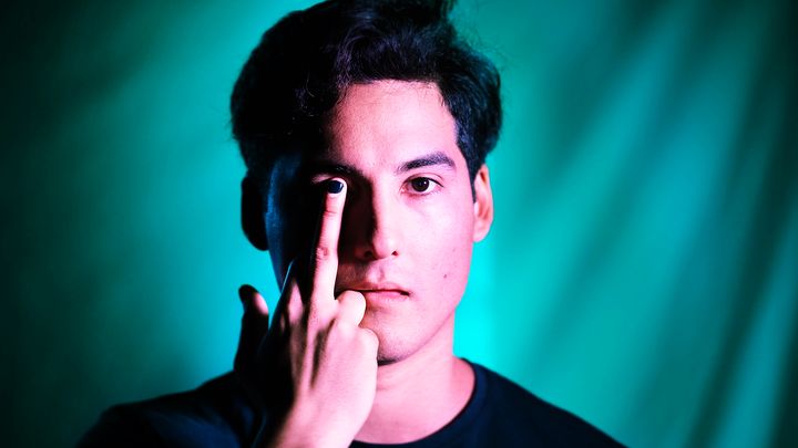 Bild på en ung man med allvarligt ansiktsuttryck som täcker ett öga med sitt finger. Bakgrund i grönblå toner.