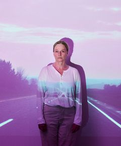 Kvinna står mot en bakgrund med projicerad landsväg.