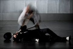 Philip Zandén ligger dramatiskt på scengolvet med en käpp i handen, iförd kostym, medan en suddig gestalt rör sig ovanför honom.