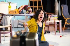 Bianca Cruzeiro sitter på golvet och skriker i intensiv scenmiljö med rekvisita omkring.