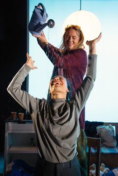 Sandra Huldt häller vatten ur en vattenkanna på Bianca Cruzeiro, båda är glada och skrattande. I bakgrunden en hängande lampa.