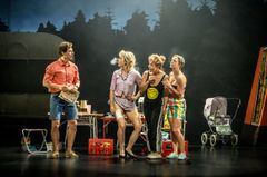 Fyra personer står på en teaterscen omgiven av rekvisita, inklusive barnvagn och campingutrustning.