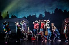 Ensemblen från "Landet utom sig" uppträder på scenen framför en husvagn och skogssilhuett.