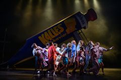 En grupp skådespelare står framför en stor rekvisita av en kaviartub på en teaterscen.