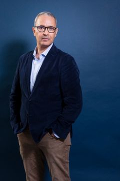 Man i kavaj och glasögon mot en blå bakgrund.