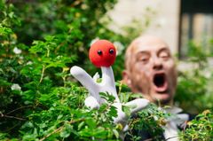 En person håller upp en vit handske med en röd boll med ögon framför ansiktet.