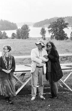 Monica Almqvist-Lovén, Helge Skoog och Claire Wikholm står på en äng vid vatten; Helge bär solhatt och Claire till höger håller honom i armen.