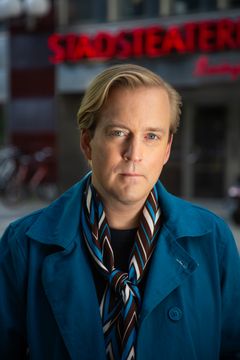 En man i blå kappa framför Stadsteatern.