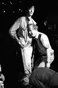 Helge Skoog och Lars Hansson står nära varandra, en skrattar med huvudet mot den andres mage; en kvinna böjer sig ned i förgrunden.