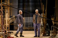 "Två män står på en scen med trä- och tygrekvisita."