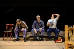 Tre män sitter på en scen. En man dricker något från en mugg, en annan skrattar, och den tredje lutar sig bakåt och dricker från en flaska.