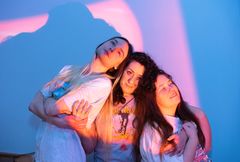 Tre personer står nära varandra mot en färgglad bakgrund.