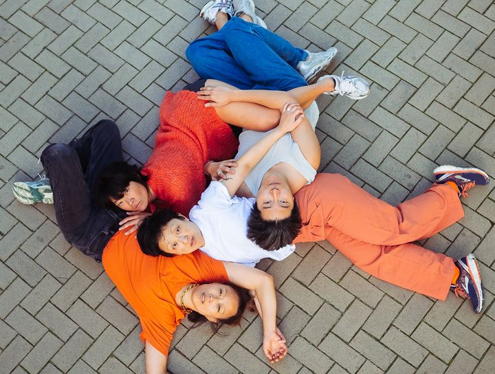 En grupp människor ligger på marken och tittar uppåt, omgivna av stenar i ett mönster.