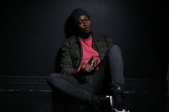 En person sitter avslappnat mot en mörk vägg.