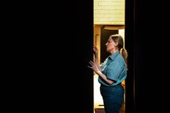 Kvinna i blå skjorta står i en smal dörröppning, scenbelyst.