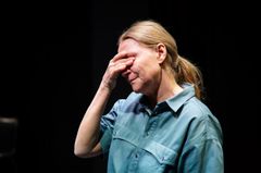 En person i blå skjorta håller handen över ansiktet på scen.