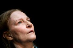 Kvinna med långt, ljusbrunt hår tittar uppåt mot en mörk bakgrund.