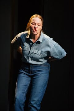 En person i blå skjorta och jeans agerar intensivt på en scen.