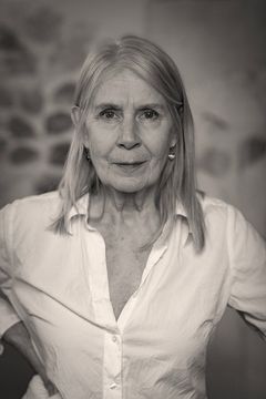 En svartvit bild av en äldre kvinna i vit skjorta som tittar direkt mot kameran.