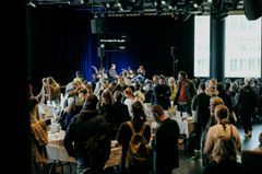 En grupp människor samlade i ett stort rum, som verkar delta i ett evenemang med flera bord och skyltar.