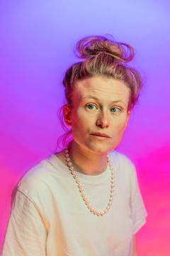Person med uppsatt hår och pärlhalsband mot en färgglad bakgrund.