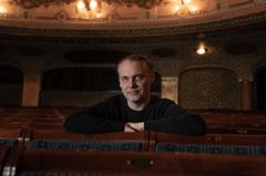 En man sitter i en tom teater, lutad över stolsryggar. Bakgrunden har dämpad belysning.